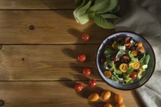 Vegetarian salad of pac choi cabbage, kiwi, tomatoes, kumquat, microgreen sprouts on a wooden