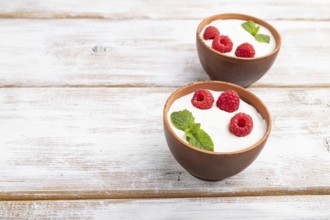 Yogurt with raspberry in clay cups on white wooden background. Side view, copy space, close up