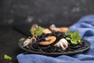 Black cuttlefish ink pasta with shrimps or prawns and small octopuses on black concrete background