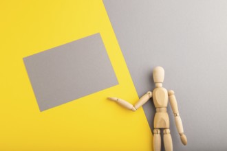 Wooden mannequin holding gray blank poster on gray and yellow pastel background. copy space,