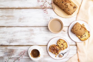 Homemade cake with raisins, almonds, soft caramel and a cup of coffee on a white wooden background