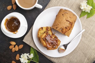 Homemade cake with raisins, almonds, soft caramel and a cup of coffee on a black concrete