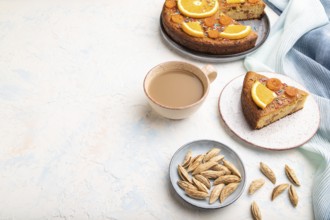 Orange cake with almonds and a cup of coffee on a white concrete background and blue linen textile.