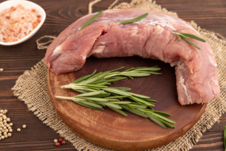 Raw pork with herbs and spices on a wooden cutting board on a brown wooden background. Side view,