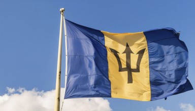 The Barbados flag flutters in the wind, isolated against a blue sky