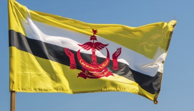 The flag of Brunei flutters in the wind, isolated against a blue sky