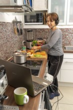 Woman, mid-50s, works from home, with laptop and communicates with colleagues via headset, home