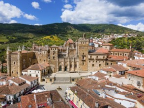 Aerial view of an old monastery with red roofs and surrounding hills under a blue sky in Spain. The