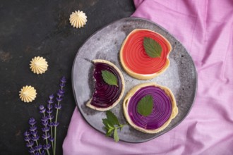 Sweet tartlets with jelly and milk cream with cup of coffee on a black concrete background and pink