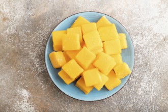 Dried and candied mango cubes on blue plate on brown concrete background. Top view, flat lay, close