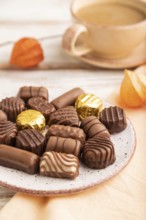 Chocolate candies with cup of coffee and physalis flowers on a white wooden background and orange