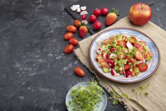 Vegetarian fruits and vegetables salad of strawberry, kiwi, tomatoes, microgreen sprouts on black