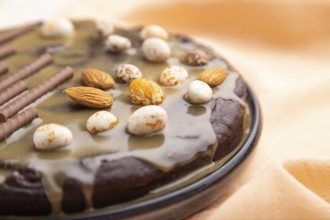 Homemade chocolate brownie cake with caramel cream and almonds with cup of coffee on a white