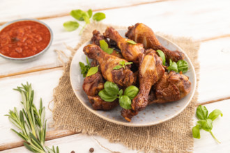 Smoked chicken legs with herbs and spices on a ceramic plate with linen textile on a white wooden