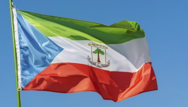 The flag of Equatorial Guinea flutters in the wind, isolated against a blue sky