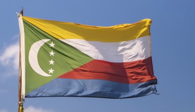 The flag of the Comoros flutters in the wind, isolated against a blue sky