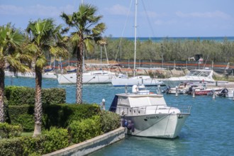 Leisure boats at quay in canal and with palm trees and holiday homes in Lido di Policoro resort,