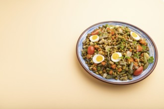 Mung bean porridge with quail eggs, tomatoes and microgreen sprouts on a pastel orange background.