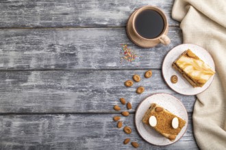 Honey cake with milk cream, caramel, almonds and a cup of coffee on a gray wooden background and