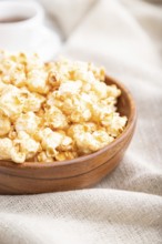 Popcorn with caramel in wooden bowl and a cup of coffee on a white wooden background and linen