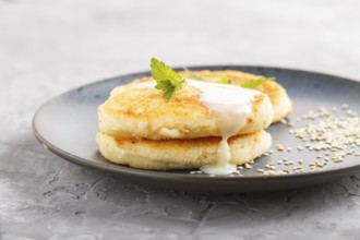 Cheese pancakes on a blue ceramic plate with milk sauce on a gray concrete background. side view,