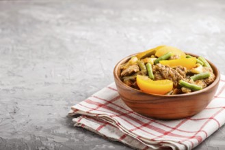 Fried pork with peaches, cashew and green beans in a wooden bowl on a gray concrete background.