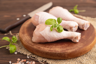 Raw chicken legs with herbs and spices on a wooden cutting board on a brown wooden background and