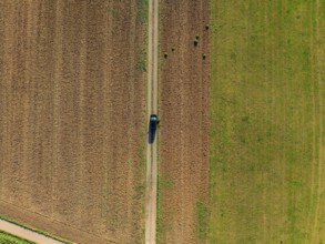 Aerial view of a car on a rural road between fields painted in green and brown colours, car