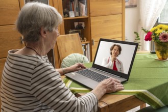 Symbolic image of telemedicine, patient speaking to a doctor in a video conference from home