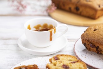 Homemade cake with raisins, almonds, soft caramel and a cup of coffee on a white wooden background.