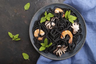 Black cuttlefish ink pasta with shrimps or prawns and small octopuses on black concrete background