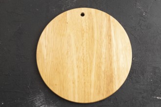 Empty round wooden cutting board on black concrete background. Top view, flat lay