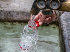 Water fountain, a woman fills drinking water into a small plastic bottle, Munich, Bavaria, Germany,