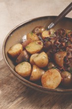 A bowl of perfectly roasted potatoes is served with caramelized onions and sprinkled with fresh