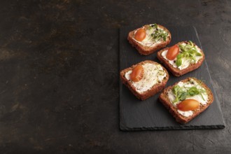 Red beet bread sandwiches with cream cheese, tomatoes and microgreen on black concrete background.