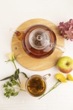 Red tea with herbs in glass teapot on white wooden background. Healthy drink concept. Top view,