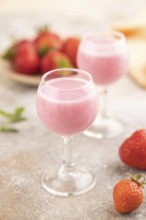 Sweet strawberry liqueur in glass on a gray concrete background and orange textile. side view,