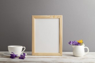 Beige wooden frame mockup with snowdrop crocus flowers and white coffee cup on gray paper