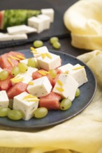 Vegetarian salad with watermelon, feta cheese, and grapes on blue ceramic plate on black concrete