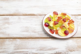 Various fruit jelly candies on plate on white wooden background. side view, copy space