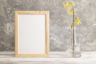 Wooden frame with yellow trout lily or dogtooth violet flowers in glass on gray concrete background