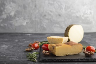 Smoked cheese and various types of cheese with rosemary and tomatoes on black slate board on a