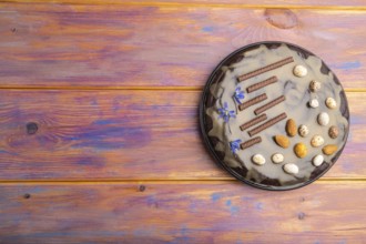 Homemade chocolate brownie cake with caramel cream and almonds on a colored wooden background. top