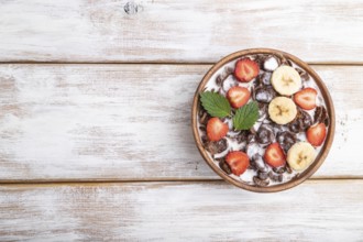 Chocolate cornflakes with milk and strawberry in wooden bowl on white wooden background. Top view,