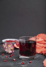 Glass of pomegranate juice on a black concrete background with red textile. Side view, close up,