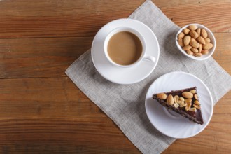 Chocolate cake with caramel, peanuts and almonds on a brown wooden background. cup of coffee, top