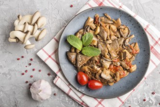 Fried oyster mushrooms with tomatoes on gray concrete background. Top view, close up