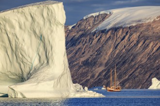 Sailing boat, ship in fjord in front of large icebergs and mountains, evening light, Scoresby