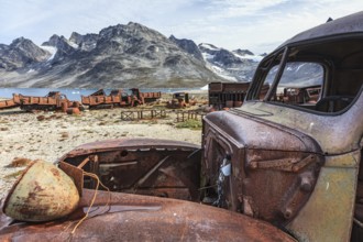 Rusted car and oil drums in front of steep mountains, remains of a US airbase from the Second World