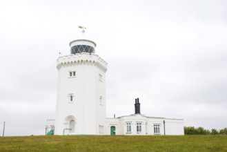 A white lighthouse stands in front of an overcast sky on a green meadow, South Foreland Lighthouse,